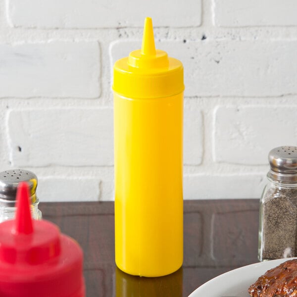 A yellow Choice wide mouth squeeze bottle on a table with a plate of meat.