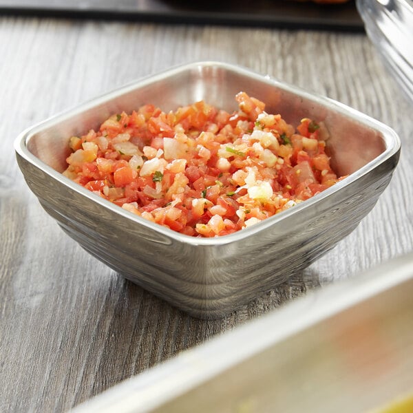 A Vollrath stainless steel bowl of chopped tomatoes and onions on a table.