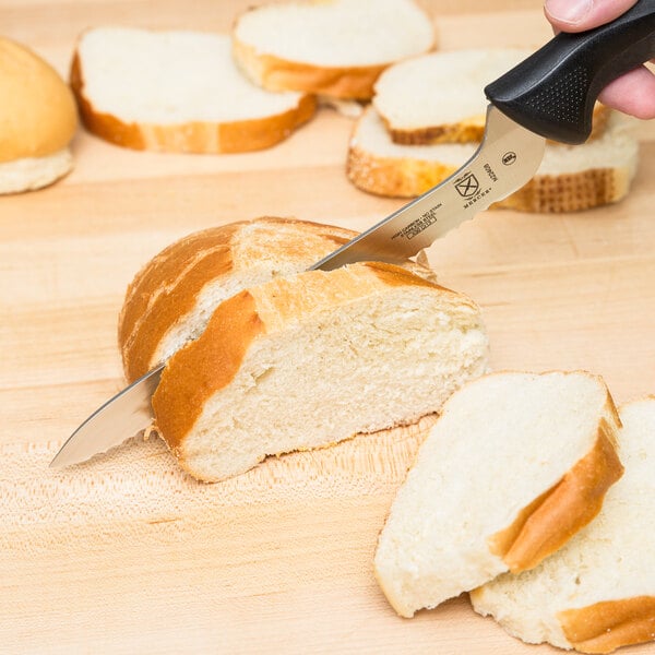 A Mercer Culinary bread knife with a yellow handle cutting a piece of bread on a cutting board.
