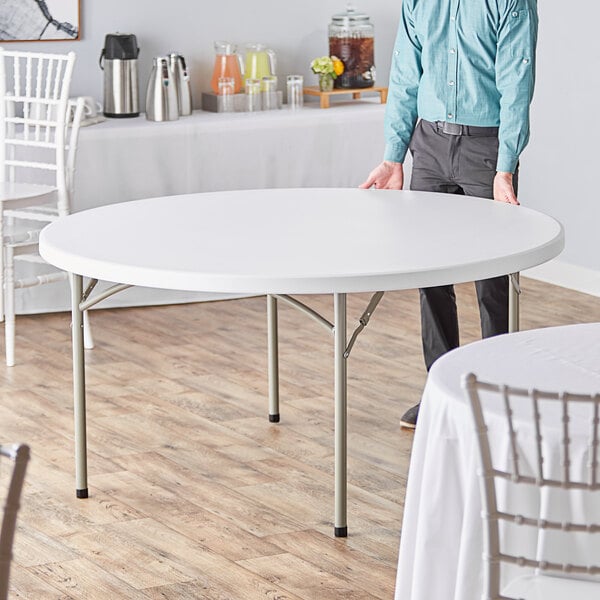 A man standing next to a Lancaster Table & Seating round folding table with a white surface.