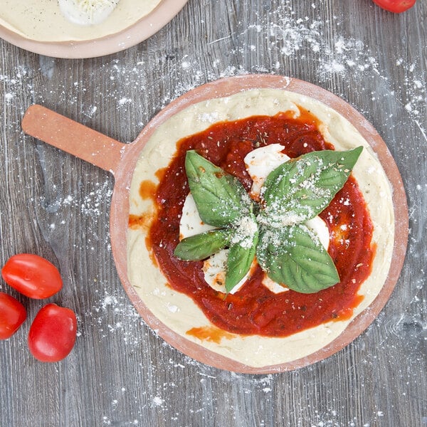 An American Metalcraft round pizza peel with a pizza topped with sauce and basil leaves.
