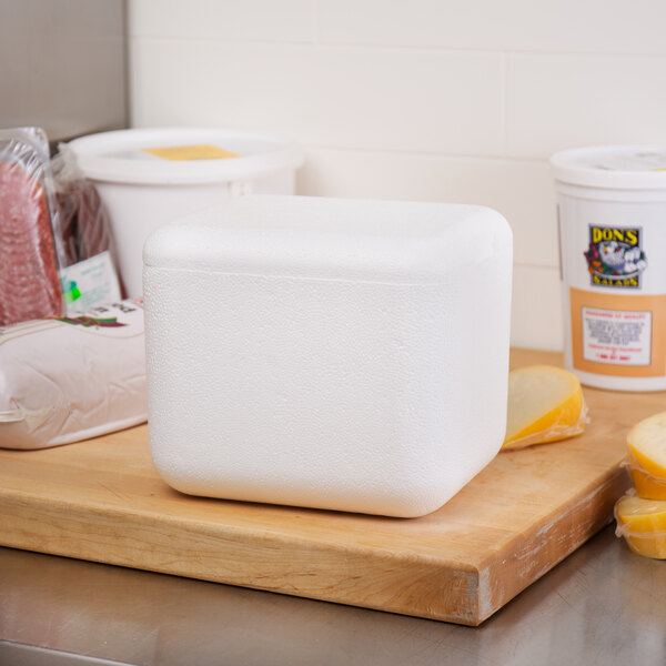 A white Nordic insulated polystyrene container on a wood surface filled with food.