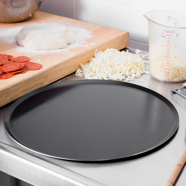 A Matfer Bourgeat black carbon steel pizza pan on a counter with a pizza on it.