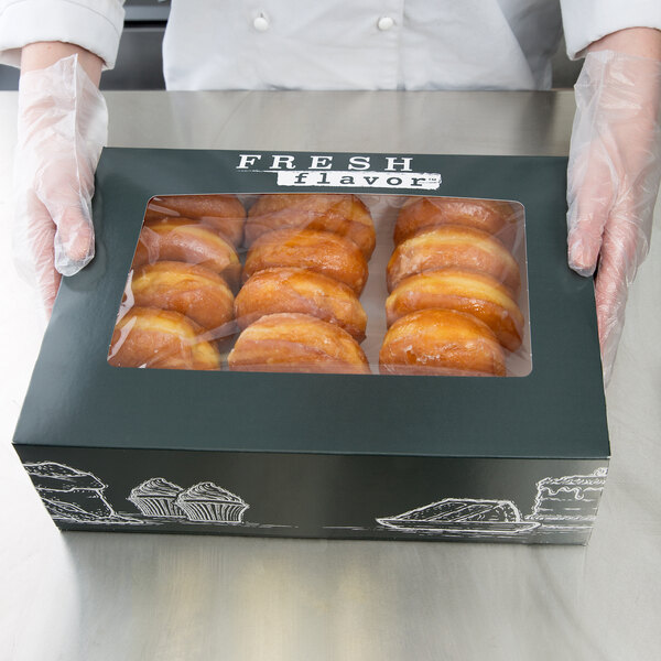 A person in gloves holding a box of doughnuts with a Fresh Print quarter sheet cake box on the counter.