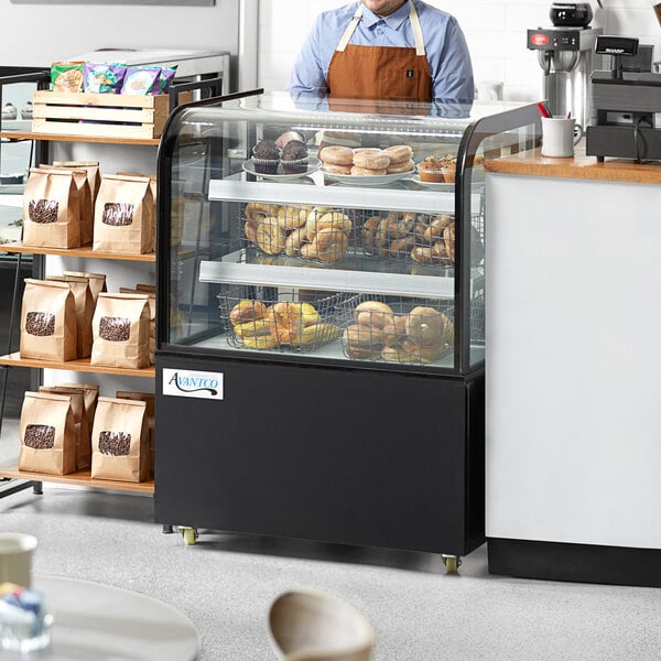 A man wearing an apron standing behind an Avantco black dry bakery display case filled with pastries.