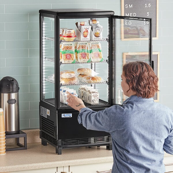 A woman taking food from an Avantco countertop display refrigerator with glass sides.