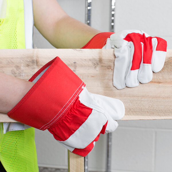 A person wearing Cordova red canvas work gloves with a piece of wood.
