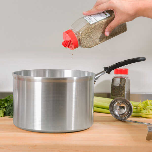 A person pouring seasoning into a Vollrath Wear-Ever Classic Select aluminum sauce pan.
