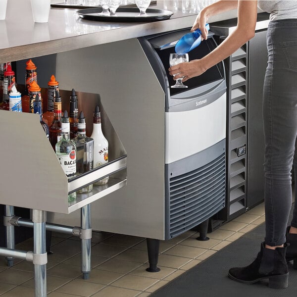 A person using a Scotsman undercounter flake ice machine to fill a cooler with ice.