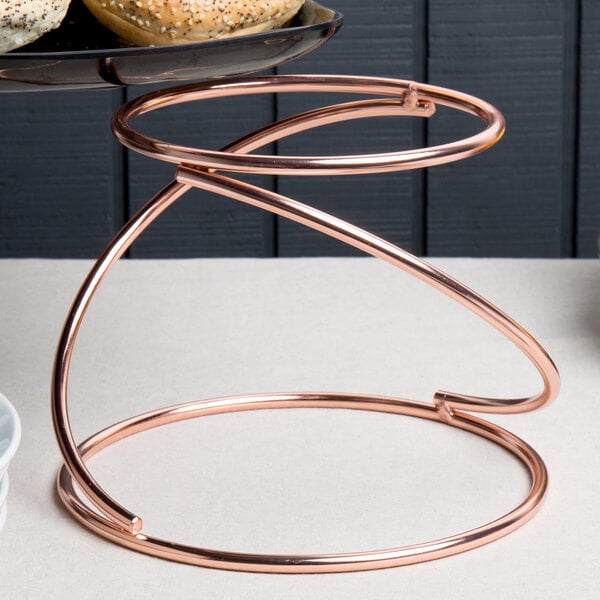 An Acopa rose gold metal display stand with a plate of donuts on it.