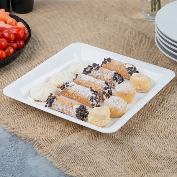 A white Fineline plastic square catering tray with pastries and cherry tomatoes on a table.