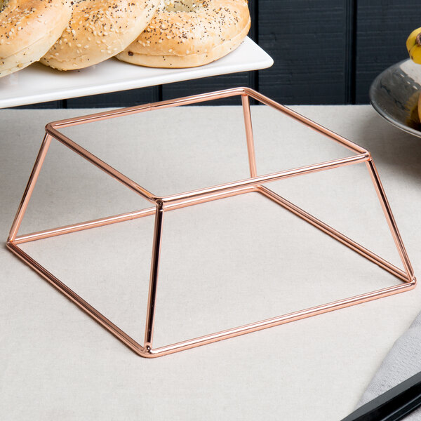 A rose gold metal Acopa display stand with a bagel on it.