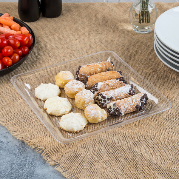 A Fineline clear plastic square cater tray with pastries and vegetables on a table.