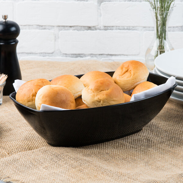 A Fineline black plastic oval bowl filled with bread rolls on a table.