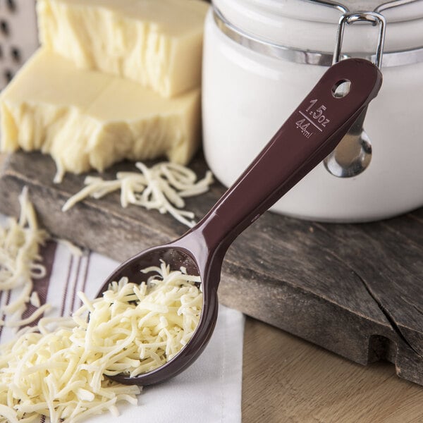 A Carlisle reddish brown portion spoon with shredded cheese on it.