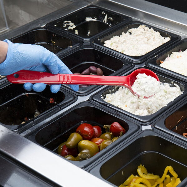 A person in a blue glove using a Carlisle red acetal long handle portion spoon to serve food from a container.