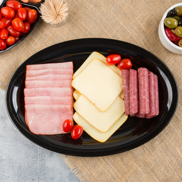 A Fineline black plastic oval catering tray with sliced meat, cheese, and tomatoes.