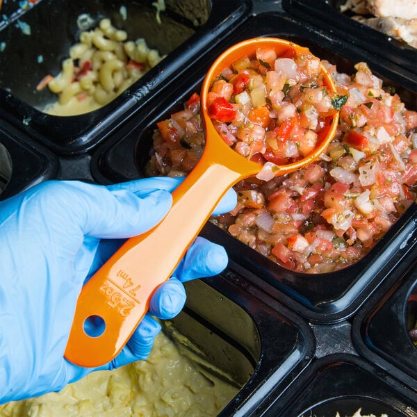 A person in a blue glove using a Carlisle orange plastic portion spoon to serve food.