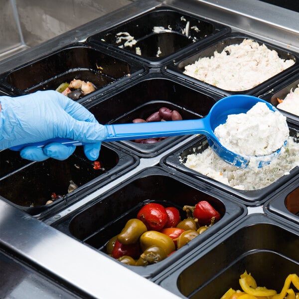 A person in blue gloves using a Carlisle blue acetal portion spoon to serve food from a black container.