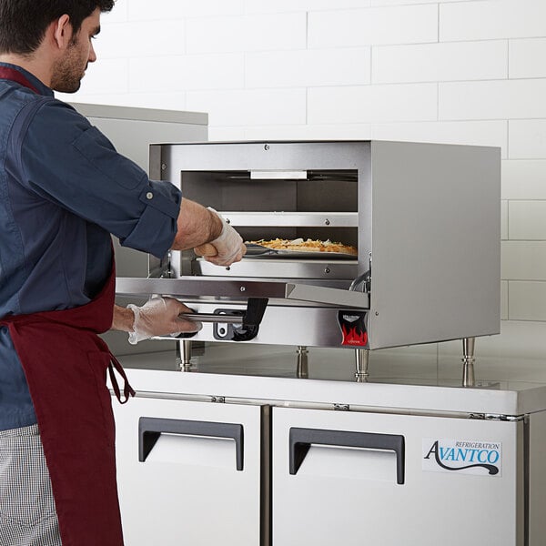 A man wearing gloves and putting pizza into a Vollrath countertop pizza oven.