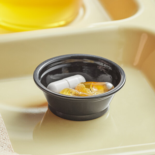 A black plastic souffle cup filled with pills and capsules.