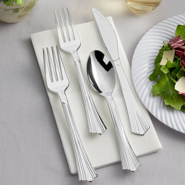 Visions silver plastic cutlery on a napkin next to a plate of salad.