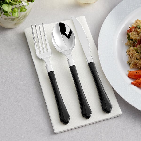 A Visions black plastic knife and fork on a napkin next to a plate of food.