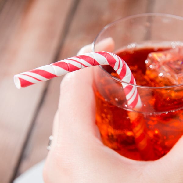 A hand holding a glass with a red and white Creative Converting paper straw in a red drink with a candy cane.
