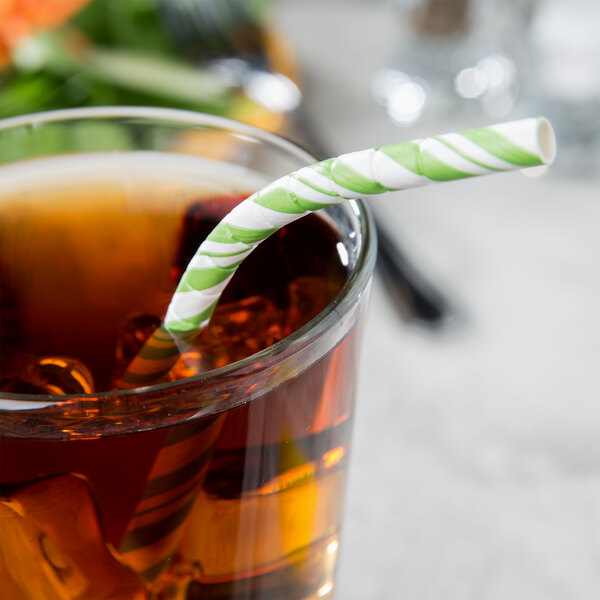 A glass with a Creative Converting Fresh Lime and white striped paper straw in it.
