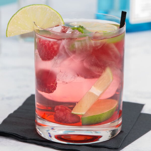 A Stolzle New York double old fashioned glass with a pink drink, fruit, and lime.