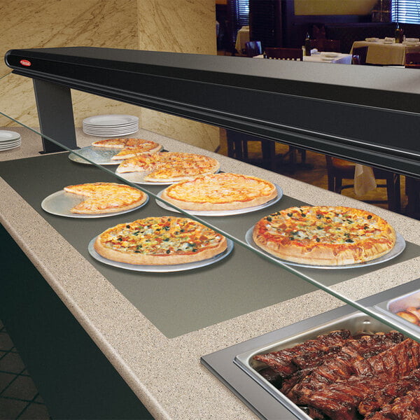 A Hatco heated shelf with pizzas on plates in a hotel buffet.