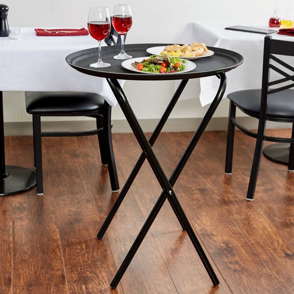 A black Lancaster Table & Seating folding tray stand with a plate of salad on it.
