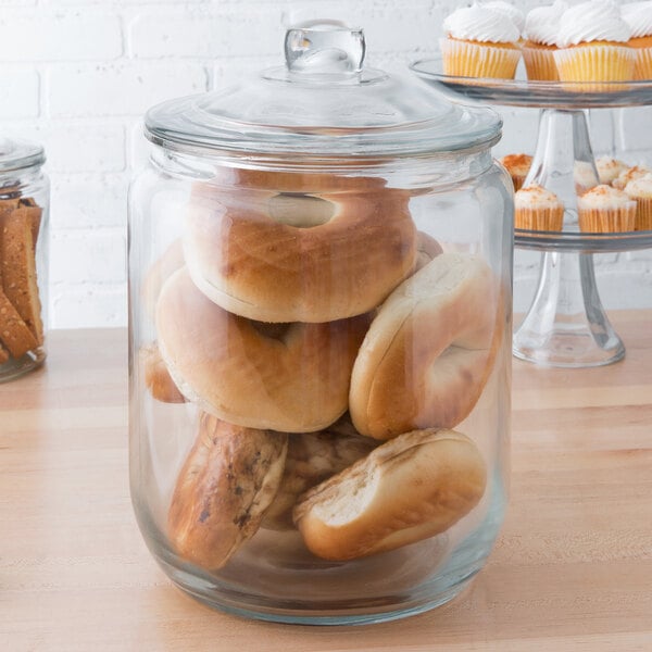 A Choice 2 gallon glass jar with a lid full of bagels and pastries on a bakery counter.