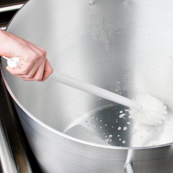 A hand holding a Carlisle white brush in a large pot.