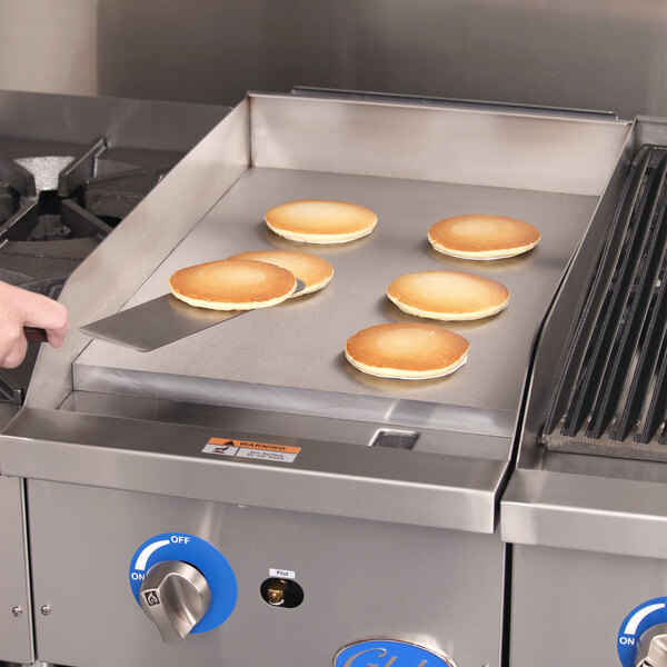 A person cooking pancakes on a Globe countertop gas griddle.