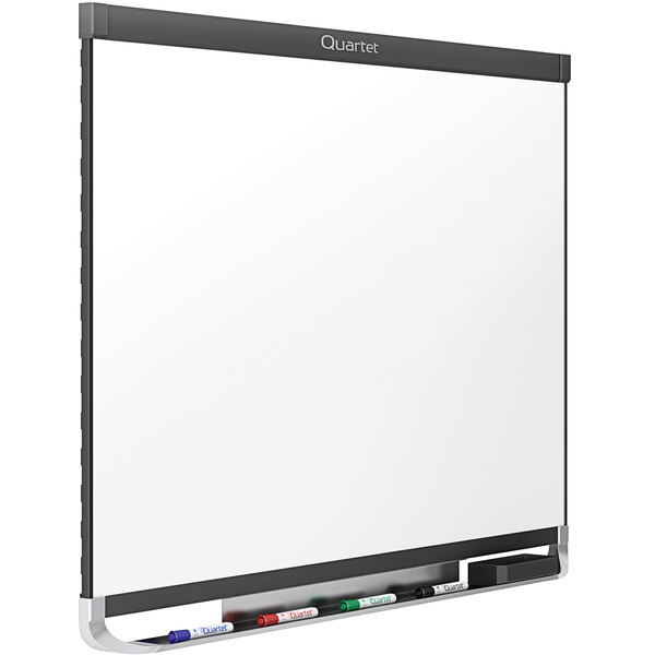 A Quartet magnetic porcelain white board with a graphite frame on a white background with markers in a marker holder.
