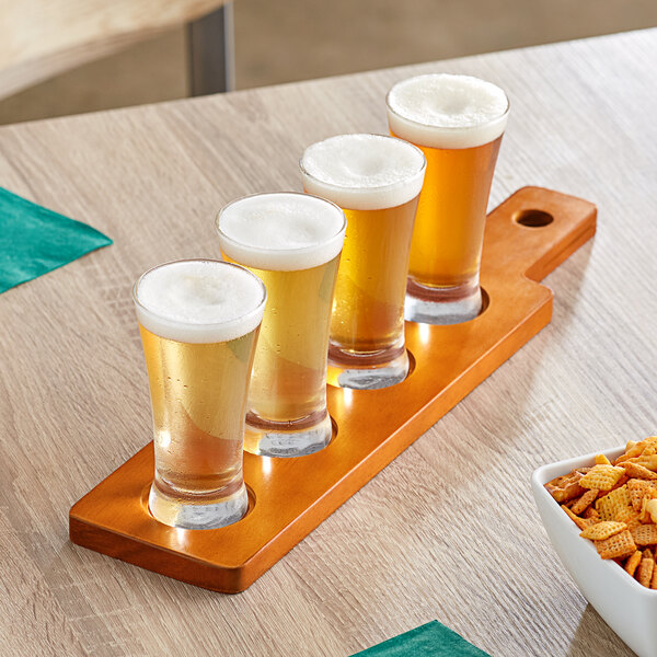 An Acopa dual-sided wooden paddle with flared pilsner glasses holding beer on a table.