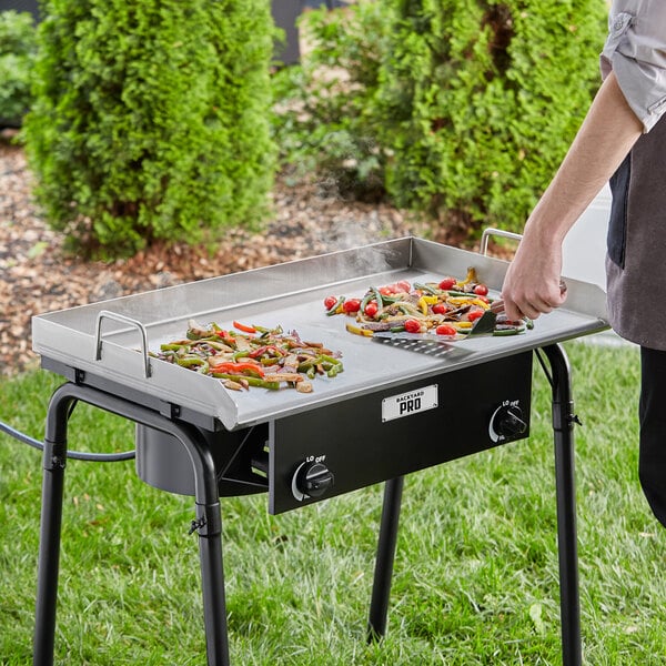 A person cooking food on a Backyard Pro stainless steel griddle plate on a table.