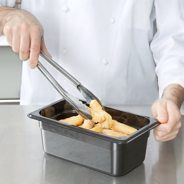 A chef using tongs to serve food from a black Cambro food pan.
