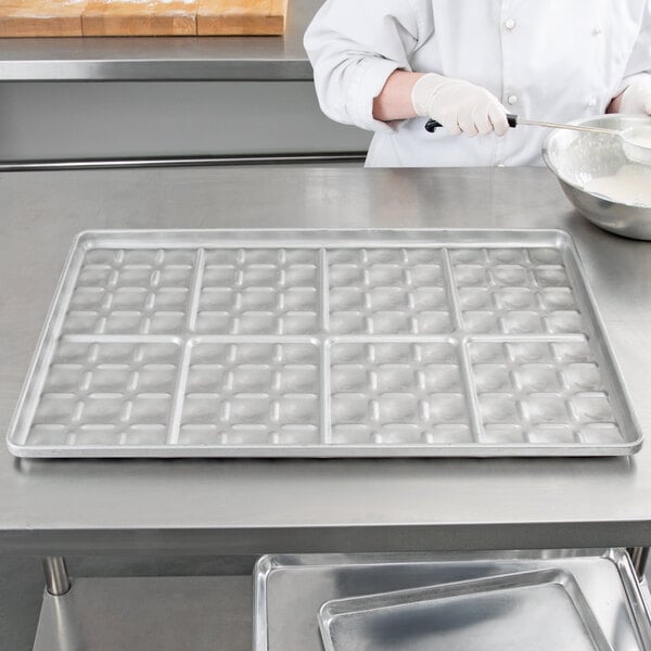 A person in a white coat using a Chicago Metallic glazed aluminized steel slider bun pan to pour white liquid into molds.