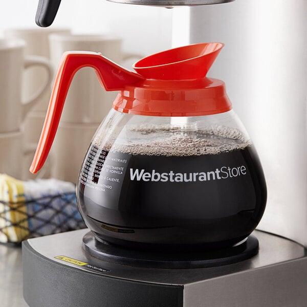 An Avantco Equipment glass coffee decanter with a red handle.