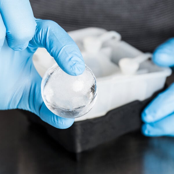 A person in blue gloves using Tablecraft black silicone sphere ice mold to make clear ice spheres.