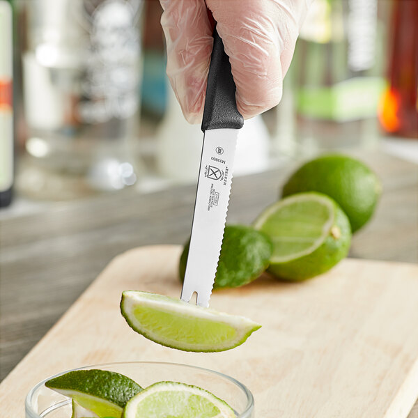 A Mercer Culinary Millennia tomato knife cutting into a lime to make a wedge.