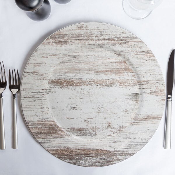 A white Charge It by Jay melamine charger plate with a faux wood rim and silverware on it.