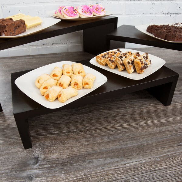A Tablecraft black painted wood riser set with trays of desserts on a table.