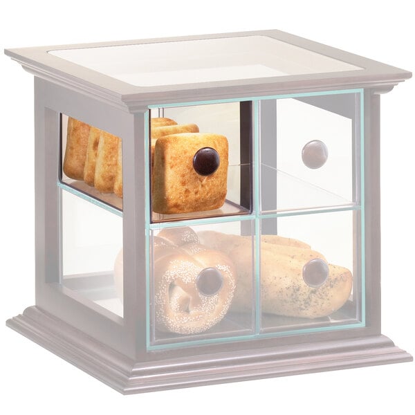A close-up of a clear drawer with a brown knob holding bread and pastries in a glass bakery display case.