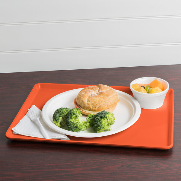 A Cambro citrus orange dietary tray with a sandwich, broccoli, and fruit on it.