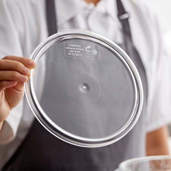 A person holding a clear lid on a Cambro clear plastic food storage container.