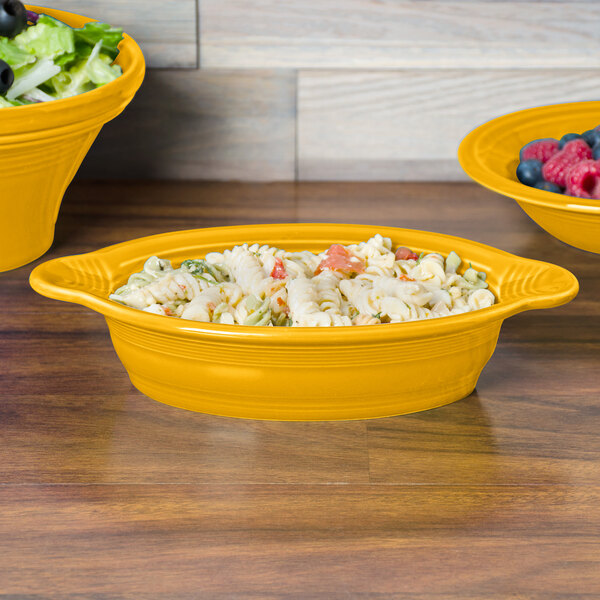 A Fiesta oval china casserole dish filled with pasta on a table with a bowl of salad and a bowl of blueberries and raspberries.