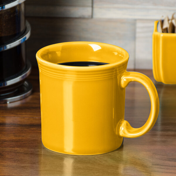 A Fiesta Daffodil yellow china mug with a handle on a table.